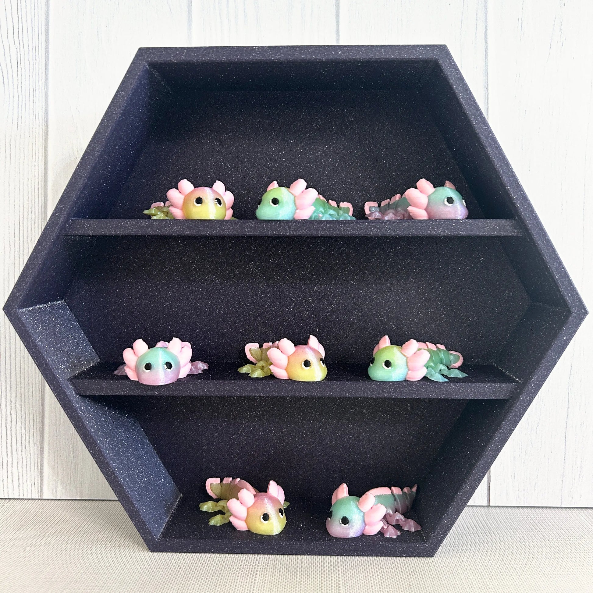 Small 3D printed axolotls on a sparkly purple shelf.