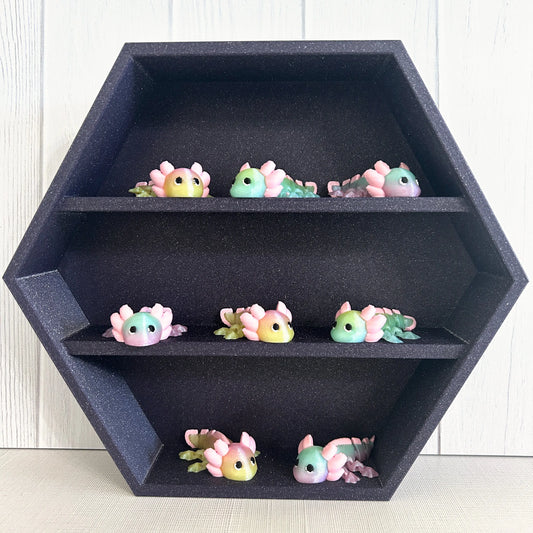Small 3D printed axolotls on a sparkly purple shelf.